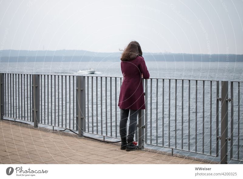 Cool, windy day. The young woman looks at the water, a boat hums by. bank rail Girl Woman ship Water Lake River Vantage point diagonal Wind chill Open watch