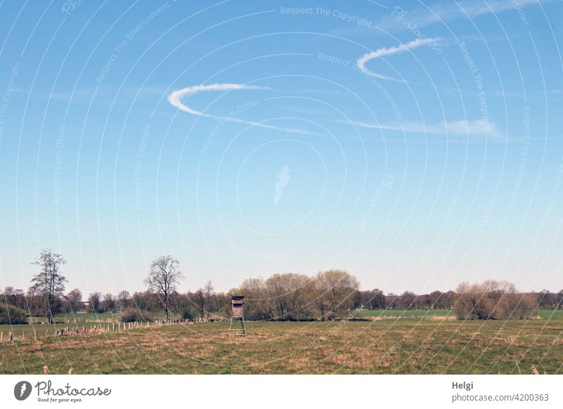 two arc-shaped condensation trails in the blue sky above a meadow with a high seat and trees Landscape Nature Meadow Hunting Blind Sky Vapor trail arched Tracks