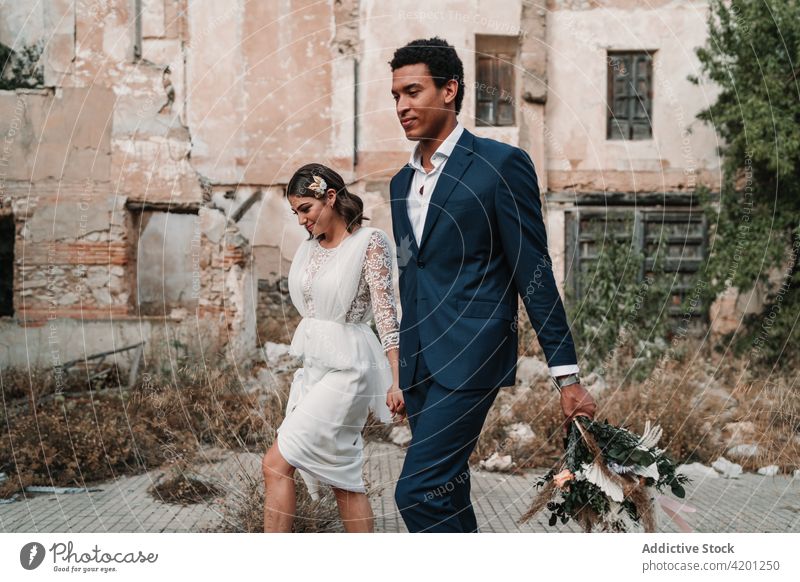 Content diverse newlywed couple walking on pavement against old building love relationship content vintage town celebrate stroll vegetate aged construction