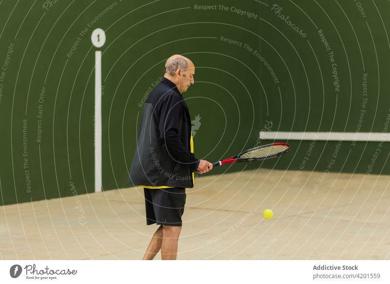 Senior man playing tennis in gym sportsman match training hit ball racket practice male athlete elderly senior aged shoot wall activity workout healthy