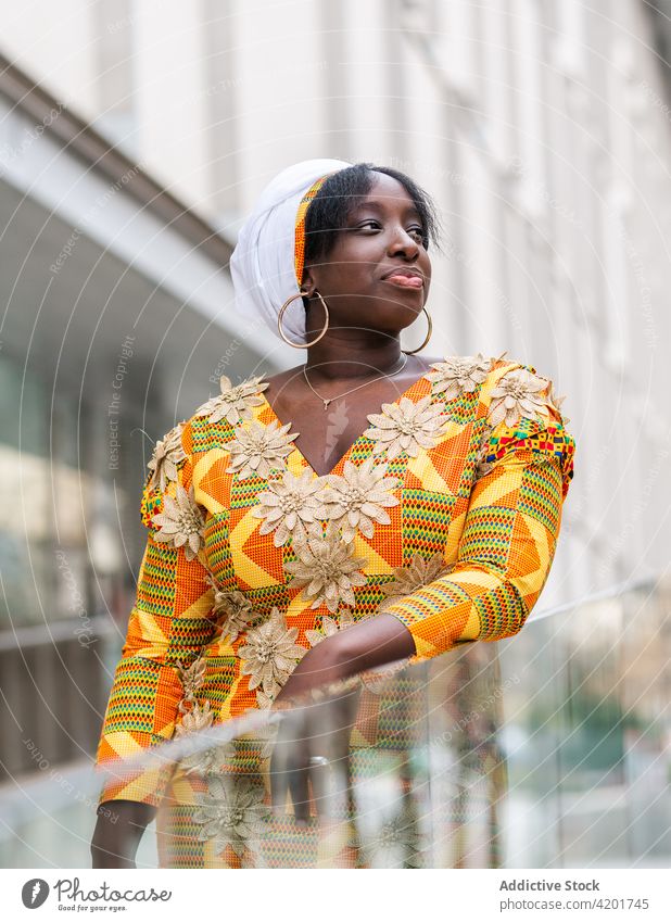 Black woman in ornamental apparel on city street style feminine elegant charming pleasant gentle portrait black african ethnic floral wear kerchief earring
