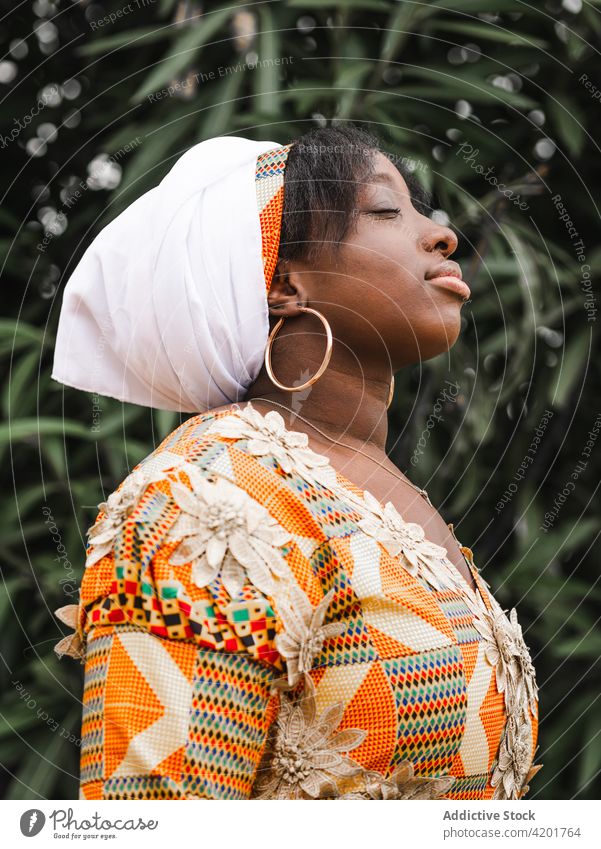 Dreamy black woman in traditional outfit in garden eyes closed dreamy breathe style charming calm portrait profile feminine elegant ornament pleasant gentle