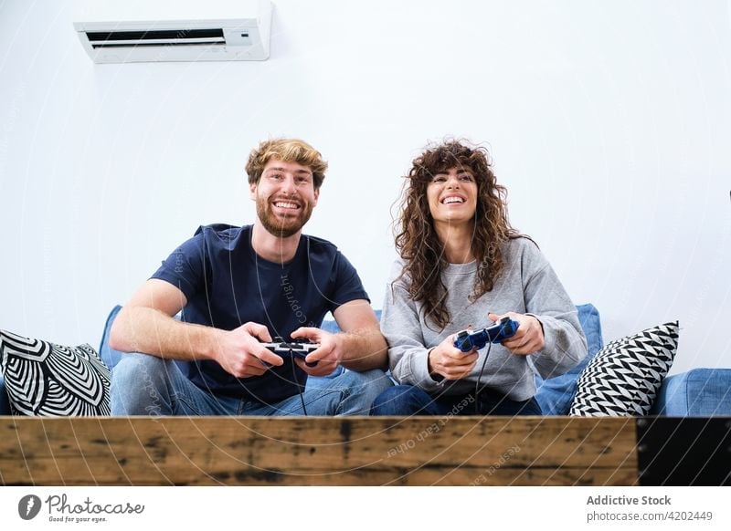 Happy Couple Sitting on the Sofa Playing Video Games, Using Controllers.  Competitive Girlfriend and Boyfriend in Love have Fun Playing in Online  Video Games at Home Together. Close-up Focus on Hands Stock