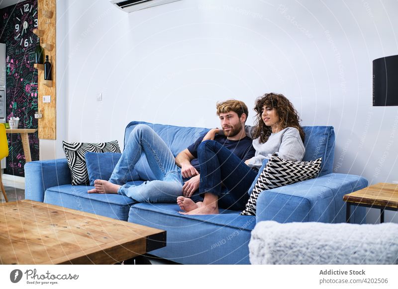 Young couple sitting on sofa and watching TV happy couch together relationship embrace love hug cheerful romantic smile bonding fondness enjoy relax girlfriend