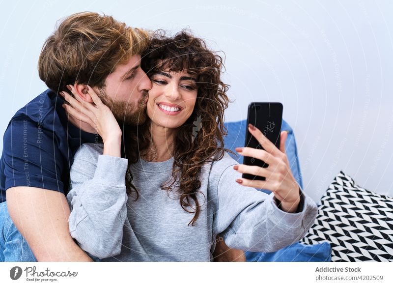 Happy couple taking selfie on smartphone happy together kiss cheerful smile love self portrait mobile casual using moment hug embrace memory cellphone bonding