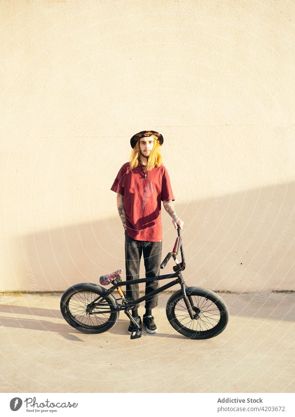 Tattooed biker with BMX bicycle on pavement trial hipster bmx sport individuality cool hand in pocket man modern style creative design vehicle bicyclist athlete