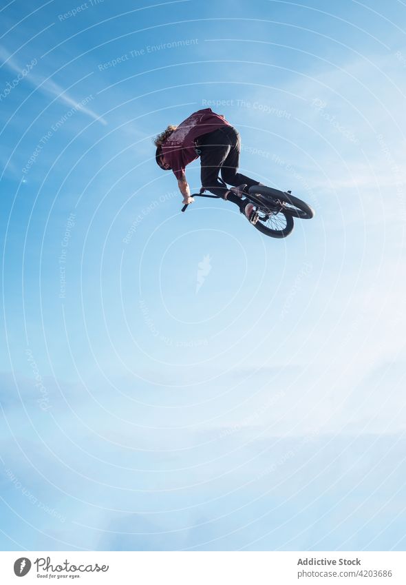 Anonymous sportsman jumping on trial bike during workout bicyclist bmx extreme freestyle adrenalin blue sky danger cloudy biker training active athlete dynamic