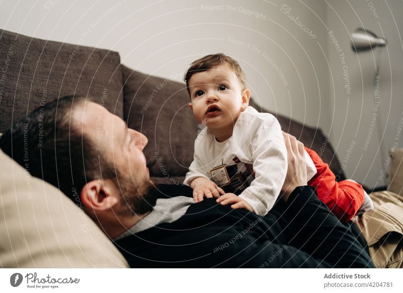 Happy man lying on sofa and playing with little son baby couch together love relationship positive hug father adorable dad happy young toddler child embrace