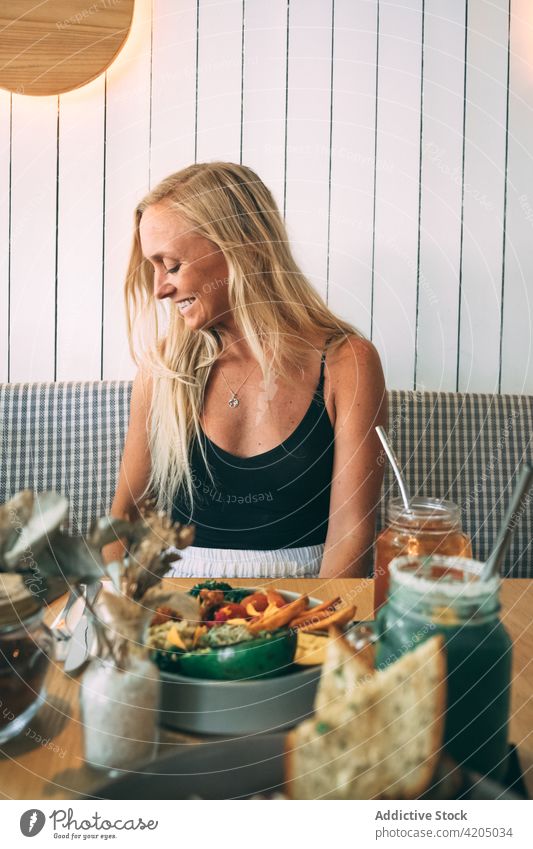 Blond woman looking to the side sitting in a restaurant blonde female drink juice caucasian food table summer cafe girl adult young eating lunch person dinner
