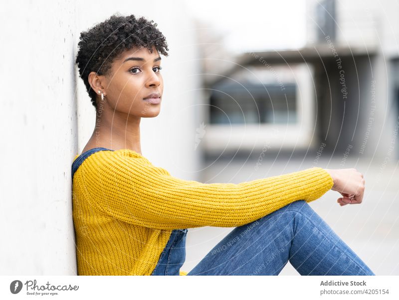 Delighted ethnic woman on street and looking away smile afro hairstyle city urban overall outfit cheerful female black african american wall lean positive