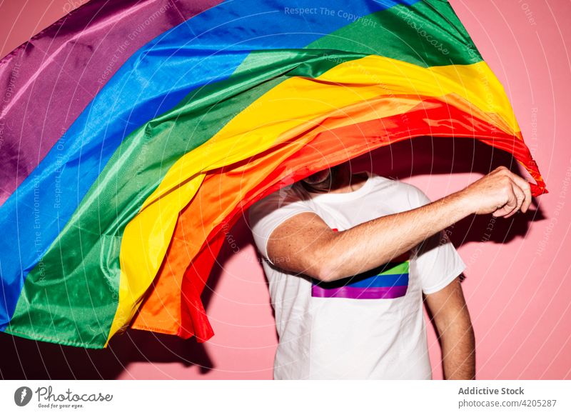 Happy man waving LGBT flag in pink studio homosexual lgbt happy gay makeup concept pride rainbow equal male unshaven red lips respect tolerance positive glad