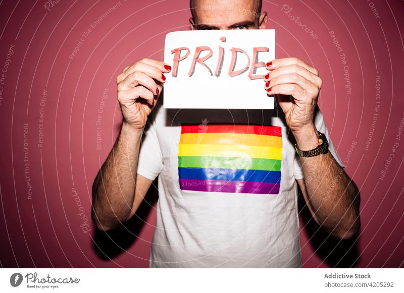 Positive gay showing paper with Pride inscription in pink studio man homosexual pride lgbtiq queer grimace cover face hide concept demonstrate support activism