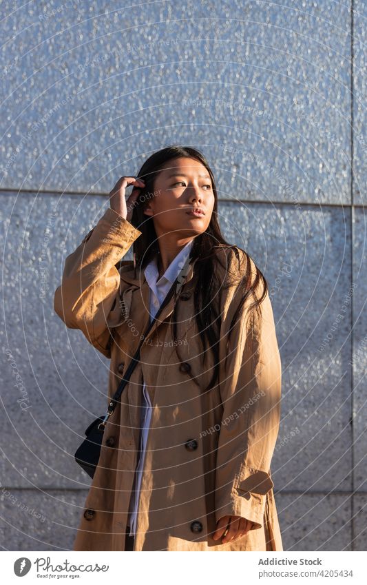 Trendy ethnic woman on city street style trendy serious confident thoughtful ponder wistful asian young dark hair contemporary long hair modern building