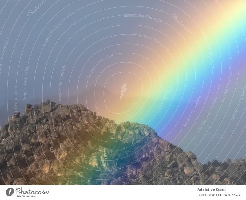 Bright rainbow over mountain range sky ridge arc landscape nature environment scenery iridescent vibrant bright vivid overcast mist rays cloudy refraction