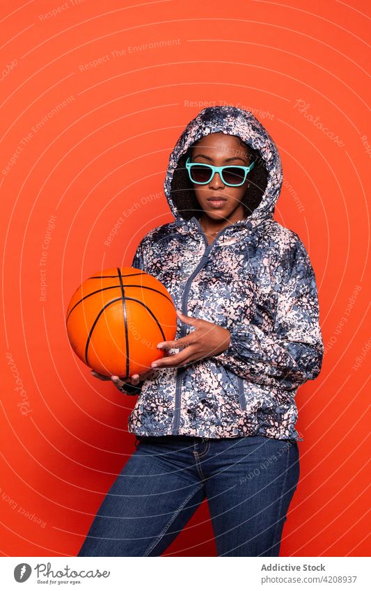 Confident black woman standing with basketball ball in studio confident style cool outfit sporty street style sunglasses appearance accessory serious trendy