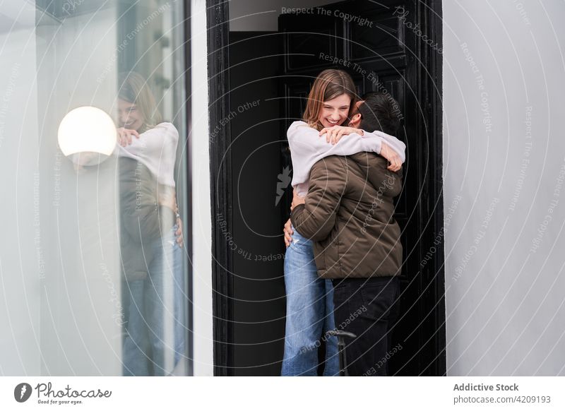 Happy woman meeting boyfriend returned from trip at doorway couple hug doorstep smile love reunion joy travel together business girlfriend young casual luggage