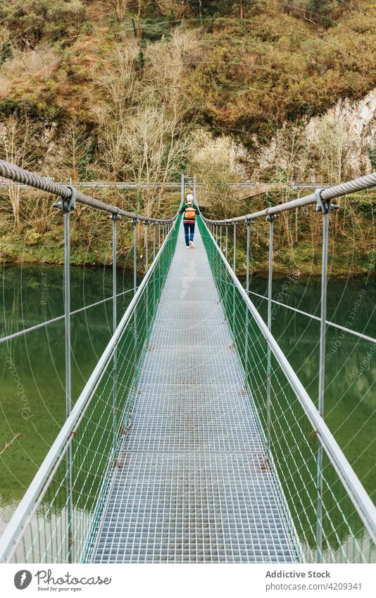 Senior traveler walking on suspension bridge against lush trees hiker route direction explore wanderlust nature woman vegetate style casual contemplate admire