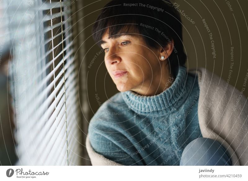 Happy middle-aged woman with nostalgic look as she gazes out the window. home 50s nostalgia pensive thoughtful thinking 40s female person brunette people