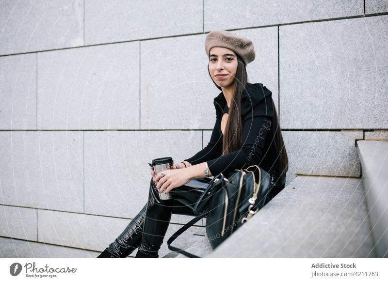 Smiling businesswoman sitting on stairs with takeaway drink city to go street enjoy style trendy female beret hat entrepreneur smile beverage outfit urban