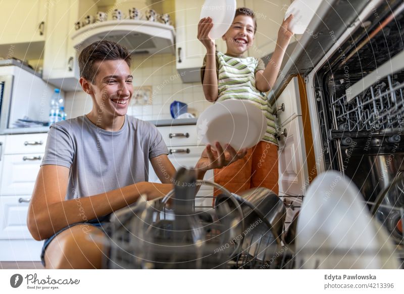 Two boys loading the dishwasher together at home washing dishes machine housework chores kitchen helping learning family brother people child son kid kids