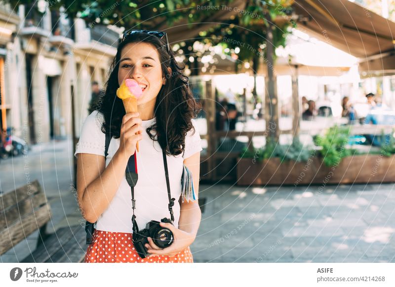 Happy young beautiful tourist woman enjoying a big ice cream eating scoop cone happy travel vacation refreshment holiday snack food city backpack camera summer