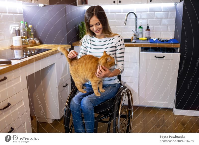 Disabled young woman in kitchen with cat on her lap wheelchair domestic life disability disabled confidence independent indoors home house people adult casual