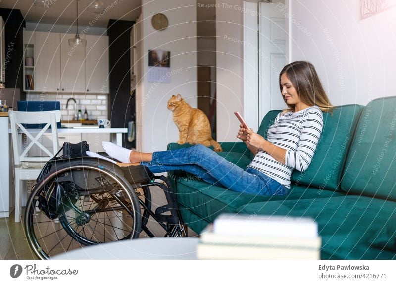 Disabled young woman using smartphone while sitting on sofa at home wheelchair domestic life disability disabled confidence independent indoors house people