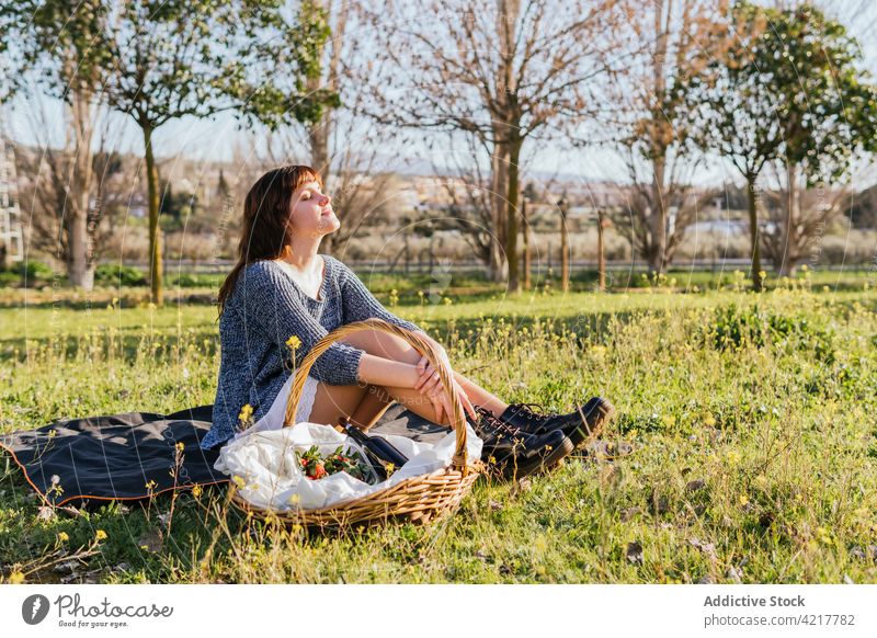 Dreamy woman enjoying picnic on sunny day spring meadow blanket dreamy carefree field female embracing knee basket happy smile serene grass rest harmony content