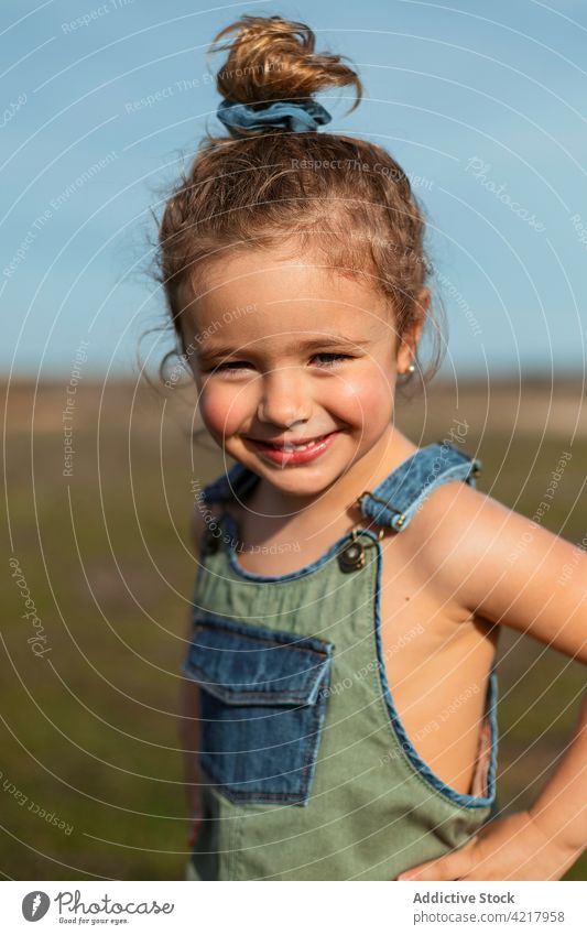 Smiling little girl standing in field in summer overall style cute outfit cheerful sunny happy childhood optimist delight smile meadow carefree glad joy sweet