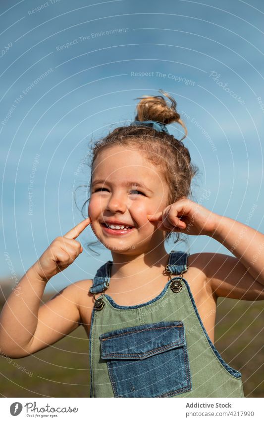 Smiling little girl standing in field in summer overall style cute outfit cheerful sunny happy childhood optimist delight smile meadow carefree glad joy sweet