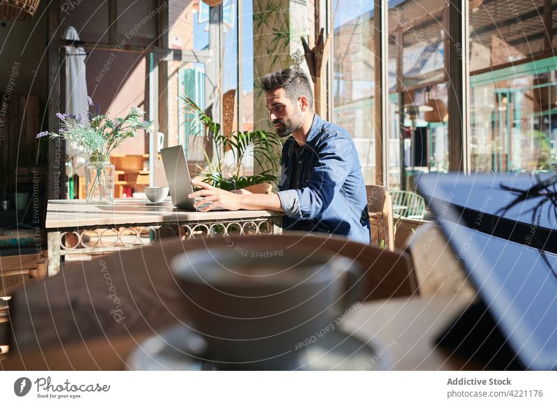 Ethnic freelancer working on laptop at restaurant table worker typing startup project independent man using gadget device netbook attentive masculine macho