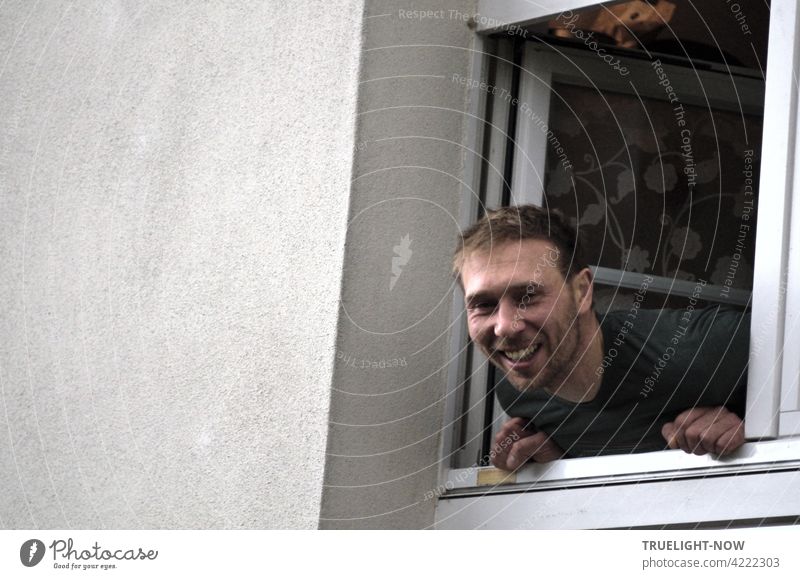The friendliest neighbor ever - a young man and father leans out of a small window laughing and looks directly into the spontaneously drawn camera of the photographer