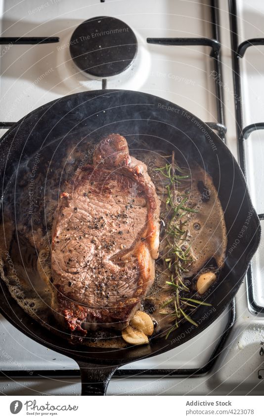 Frying pan with delicious beef steak and seasonings meat appetizing fry rosemary garlic stove gas aroma steam butter melted condiment savory tasty juicy tender