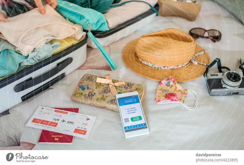 Woman preparing suitcase for vacation and mobile phone with covid green pass covid passport digital health passport woman hands on the bed holiday beach