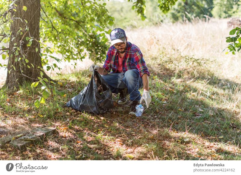 Young man picking up litter in his local park walking hiking forest grass natural countryside environment tree outside male person day outdoors autumn adult