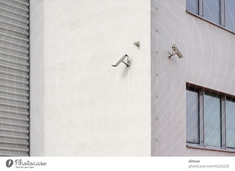 Two surveillance cameras are mounted on the corner of a functional building with windows and a roller shutter door / Security technology / Surveillance