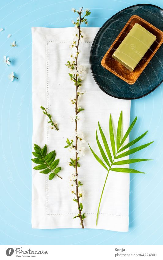 A green soap in a wooden bowl, a white towel and a flower branch on a blue background Soap Green flowering twig Towel Beauty Photography Wellness Spa Relaxation