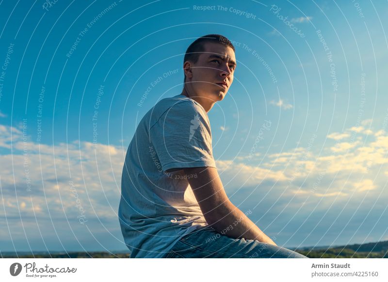seated young man looks into the distance in a beautiful landscape sitting looking sky blue summer outdoor car sunset sundown nature sunlight sunbeam romantic