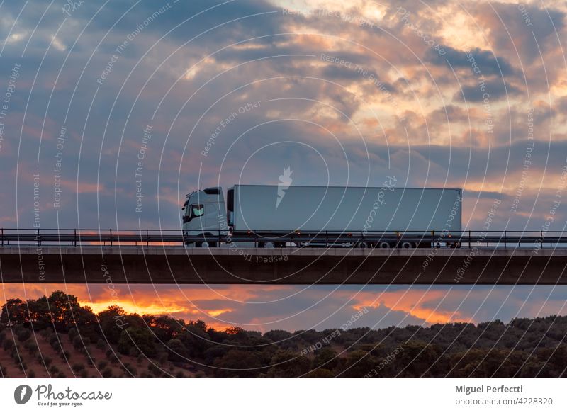 Refrigerated truck driving over a bridge with a dramatic sky in the background. road trailer transportation refrigerated sunset viaduct sunrise industry