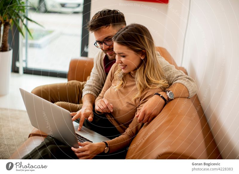 Young couple using laptop together while sitting on sofa at home adult apartment attractive boyfriend carefree caucasian comfortable computer couch day enjoying