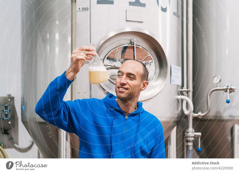 Smiling brewer with wort in flask in factory fermented analysis foam smile man small business portrait production tank fermentation work industry alcohol froth