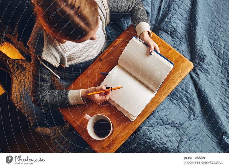 Student learning at home. Young woman making notes, reading and learning from notepad. Girl writing journal sitting in bed education indoor student working