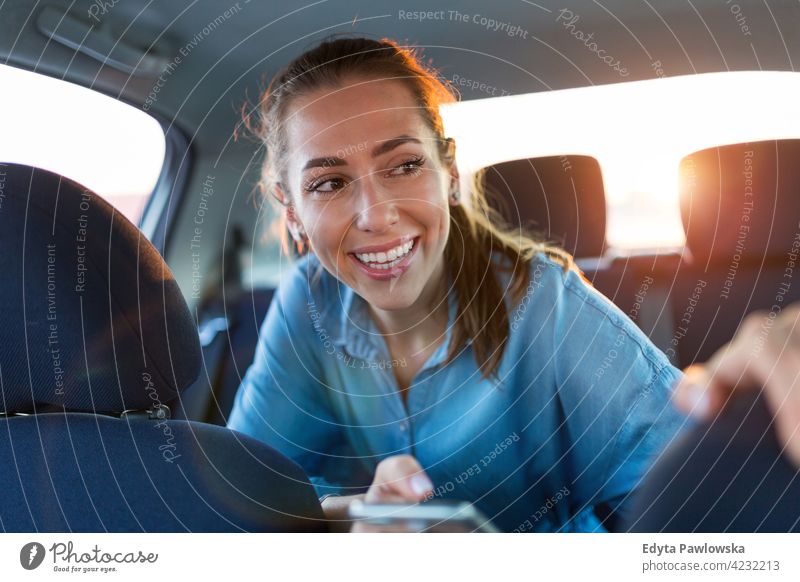 Young woman with smartphone on the back seat of a car carsharing confident smiling satisfaction female attractive beautiful young adult joy positive content