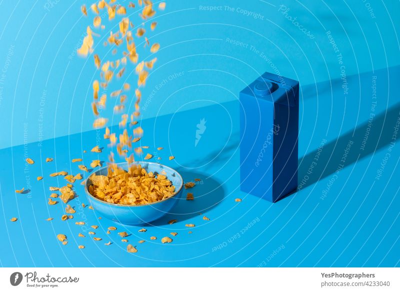 Pouring cornflakes cereal in a bowl on a blue table. Breakfast table in natural light. Abstract Accident background Blue Bottle Bowl Box Bright Carton Cereals