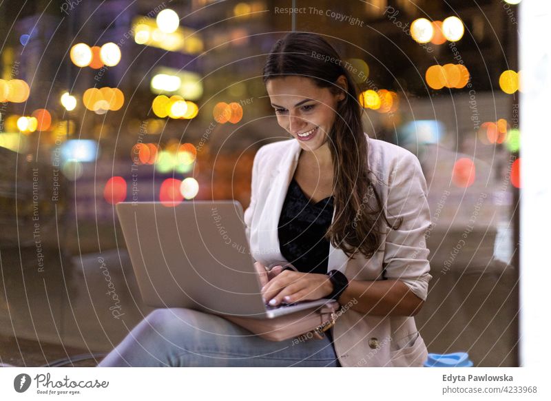 Young woman working on her laptop in the city at night urban street active people young adult casual attractive female happy Caucasian enjoying one person