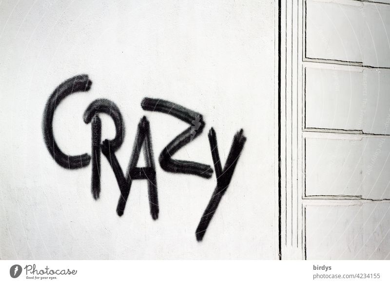 Crazy , black graffiti on white house wall crazy Characters Graffiti English unusual loopy differently universally evaluative descriptive Youth culture Word