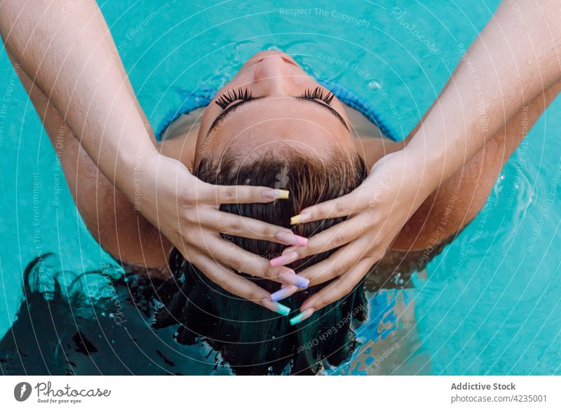 Back view female tourist in swimwear touching wet hair in pool