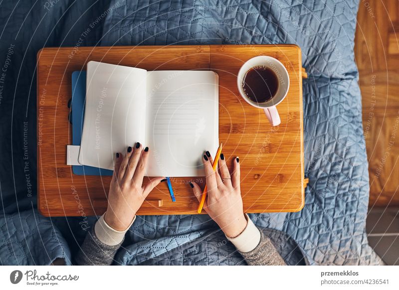 Student learning at home. Young woman making notes, reading and learning from notepad. Girl writing journal sitting in bed education indoor student working