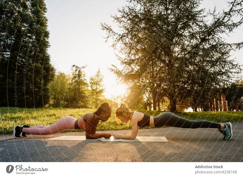 A happy female personal trainer is looking at the sportswoman who is doing  planks in a gym. Stock Photo