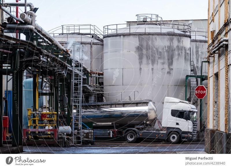 Tank truck loading in a factory next to some tanks and under pipes that give off steam. tank truck storage industry oil deposit plant industrial metal steel